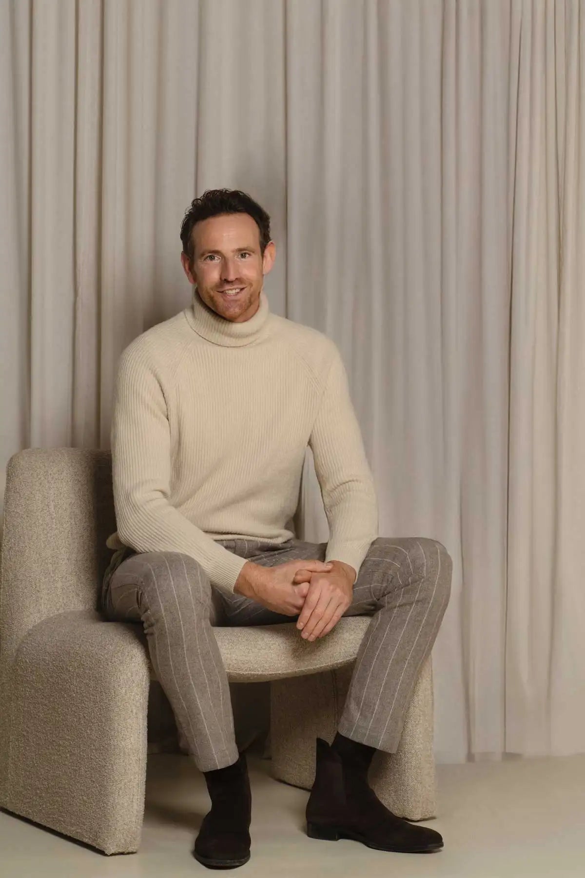 Een man die een roomkleurige geribbelde coltrui draagt.